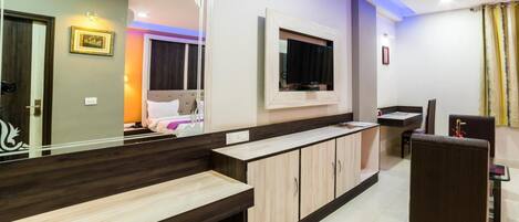 A modern hotel room with a large mirror, a TV mounted on the wall, a wooden bench, and a small table.