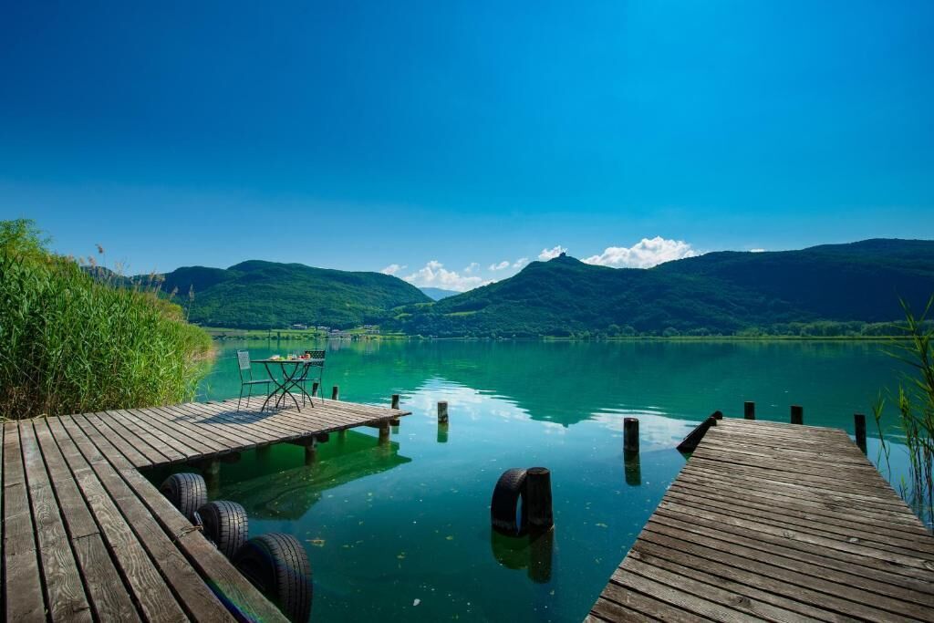 A wooden dock extending into a calm lake with a clear sky and mountains in the background.