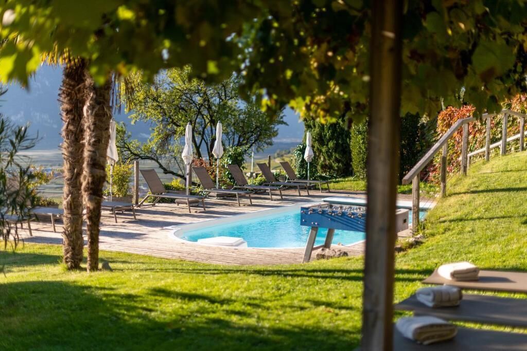 A pool area with lounge chairs and umbrellas, surrounded by greenery and a view of the landscape.
