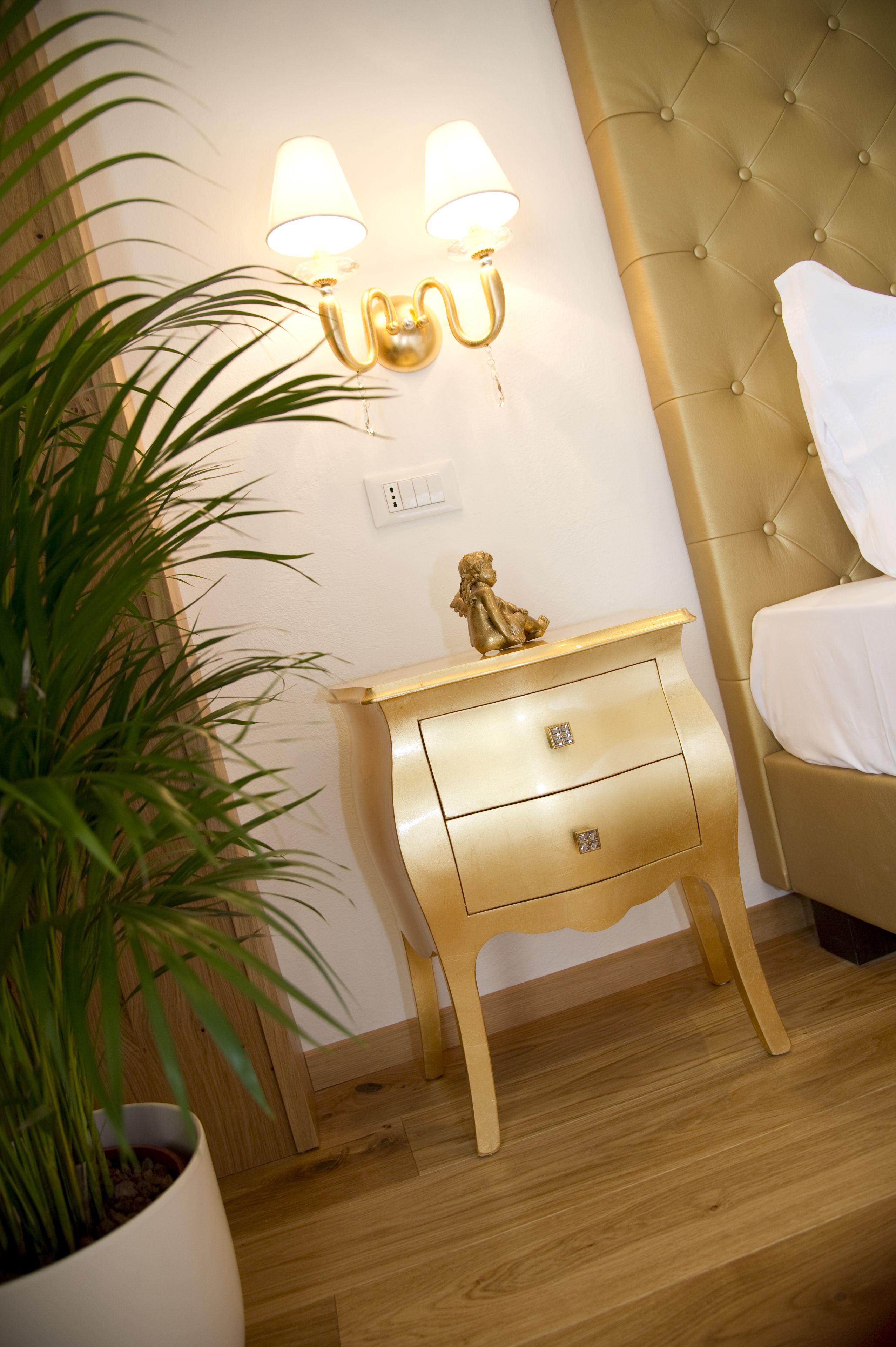 A bedroom with a bed, a nightstand with a lamp, and a potted plant.