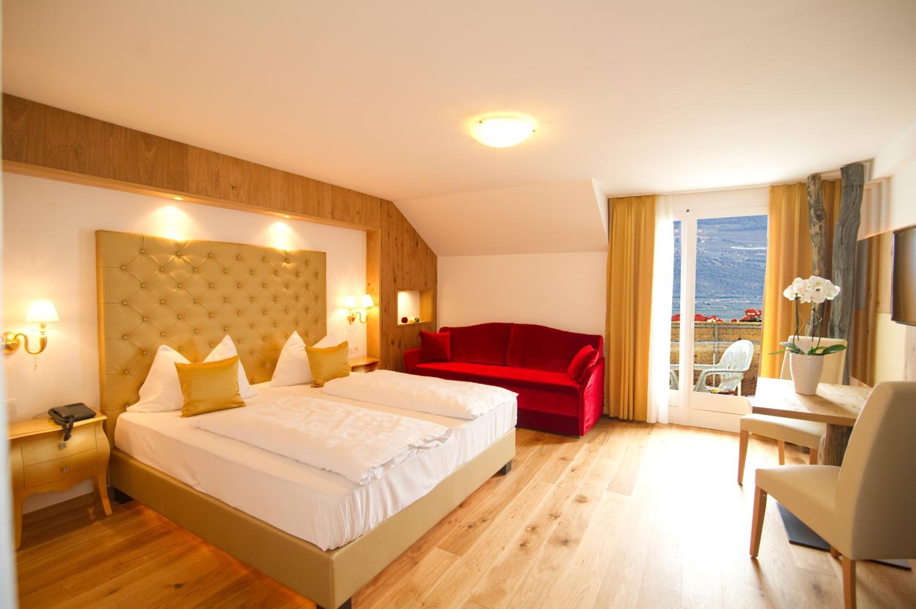 Et hotelværelse med en stor seng, en rød sofa, et lille bord med en stol og en balkon med udsigt.