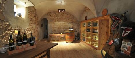Una bodega rústica con barriles de madera, un muro de piedra y un gabinete de madera que exhibe botellas.