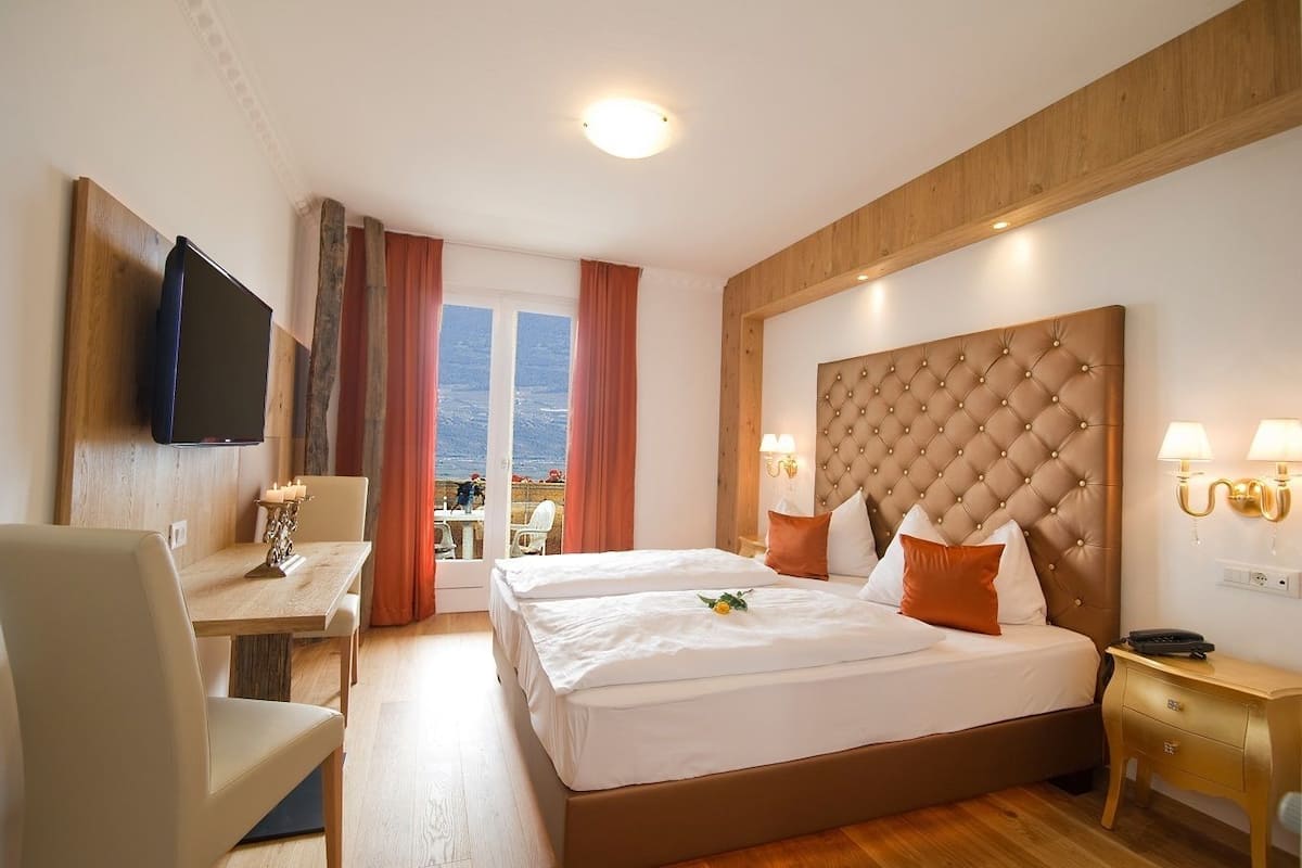 Habitación de hotel con una cama grande, un escritorio con una silla, un televisor montado en la pared y un balcón con vistas.