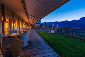 An outdoor dining area with tables and chairs, a wooden deck, and a view of mountains. - Panorama Tramin (Termeno Sulla Strada del Vino)