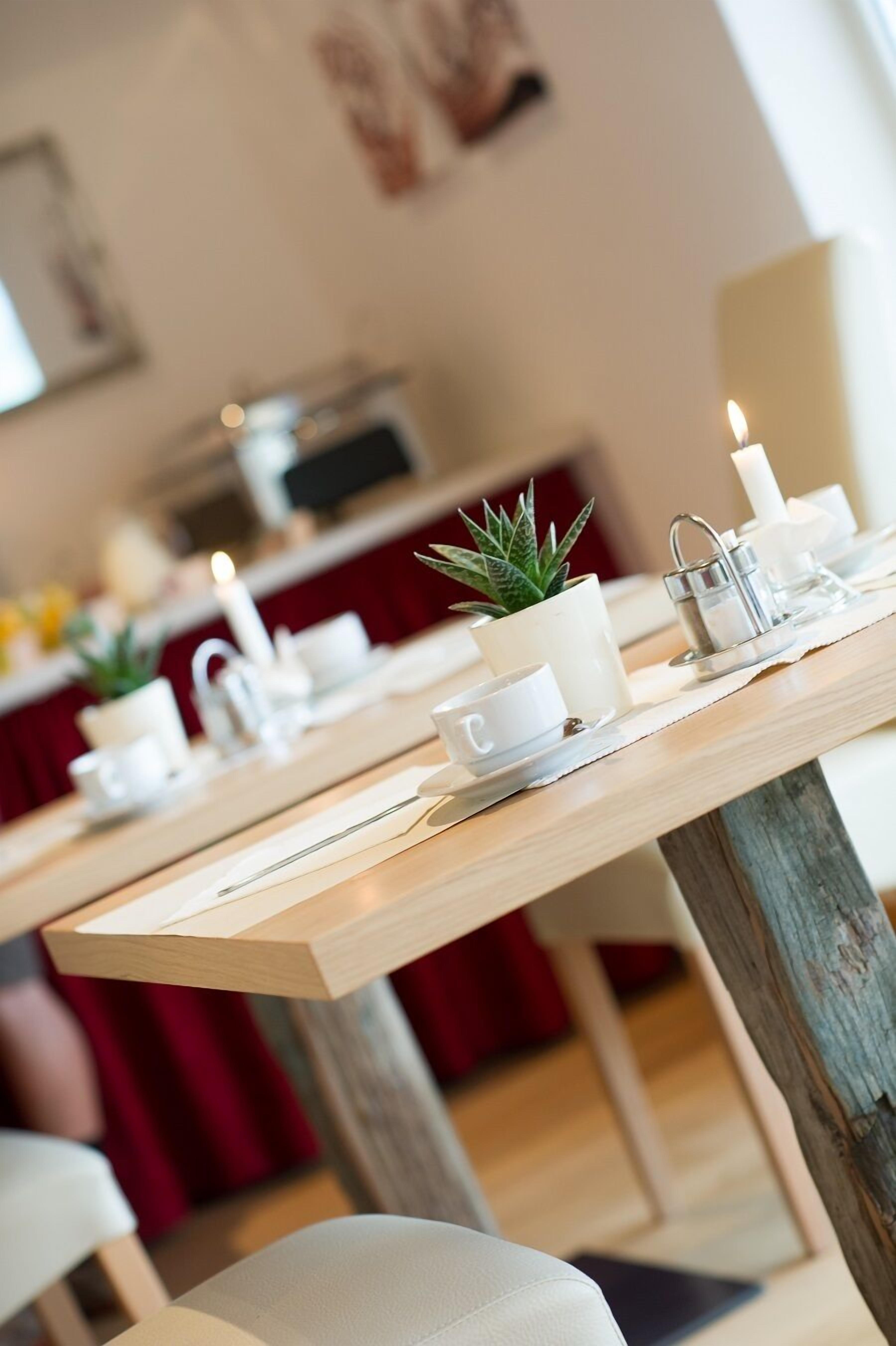 A dining area with wooden tables, white cups, a candle, and a small potted plant.