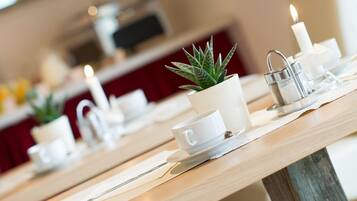 A dining area with wooden tables, white cups, a candle, and a small potted plant.