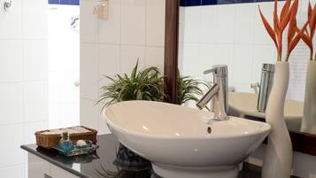 Une salle de bain avec un lavabo blanc, un miroir et une plante en pot.