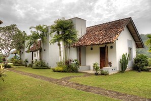 A white building with a tiled roof, surrounded by a well-maintained garden with various plants and a paved pathway. - Omatta Villa (Agalawatta)