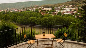 A balcony with a table and chairs overlooking a river and a town. - Apartment with terrace in Old Tbilisi (Tbilisi)