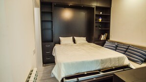 A bedroom with a bed, a nightstand, a dresser, a shelf with books, and a hanging light fixture. - Apartment with terrace in Old Tbilisi (Tbilisi)