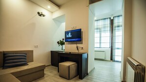 A modern living room with a sofa, a small desk, a flat-screen TV, and a window with blinds. - Apartment with terrace in Old Tbilisi (Tbilisi)