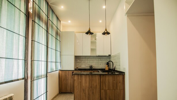 A modern kitchen with wooden cabinets, a black countertop, and pendant lighting. - Apartment with terrace in Old Tbilisi (Tbilisi)