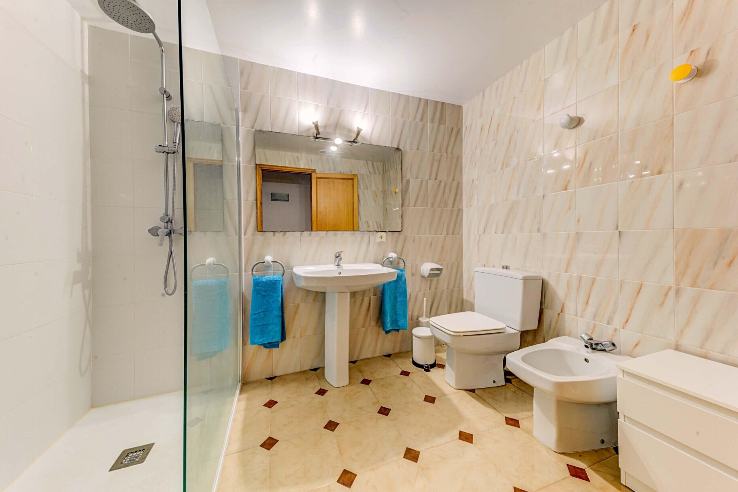 A modern bathroom with a glass-enclosed shower, a pedestal sink, a toilet, and a bidet.