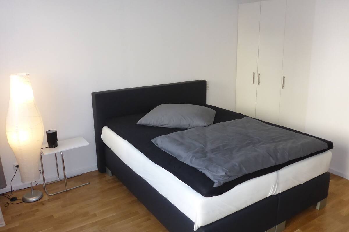 Un dormitorio con cama, mesita de noche, lámpara y armario.