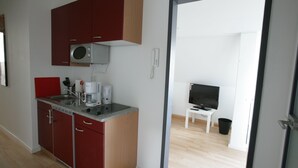 A compact kitchen with a microwave, coffee maker, and a red cabinet. A television is visible in the adjacent room.