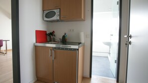 A compact kitchen with a microwave, a red cutting board, and various utensils on the counter.