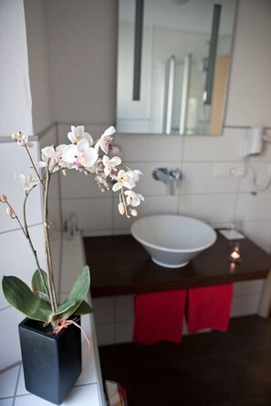 Baño con lavamanos blanco, un espejo y una orquídea en maceta.