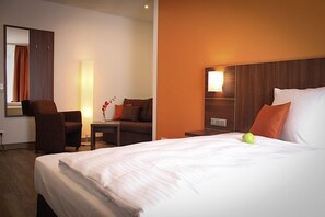 Una habitación de hotel con una cama grande, una silla, una mesita de noche y un televisor montado en la pared.