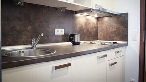 A modern kitchen with a stainless steel sink, a kettle, and a built-in stove.