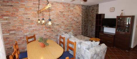 A dining area with a brick wall, wooden chairs, a round table, and hanging light fixtures.