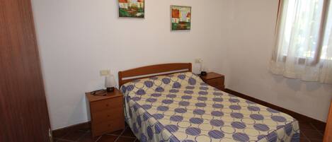Een slaapkamer met een bed, twee nachtkastjes, een wandlamp en twee aan de muur hangende schilderijen.