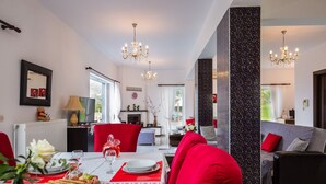 Een eetruimte met een tafel voor twee personen, rode stoelen, een kroonluchter en uitzicht op de woonkamer.