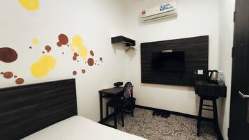 Una habitación de hotel con cama, escritorio, silla, televisor montado en la pared y un zapatero.