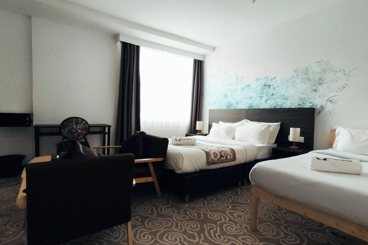 A hotel room with two beds, a desk, a chair, a small table, and a wall with a blue abstract design.