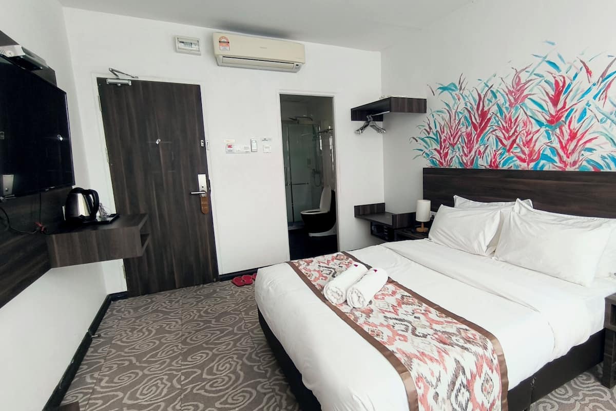 A hotel room with a bed, a TV, a desk, and a bathroom visible through an open door.