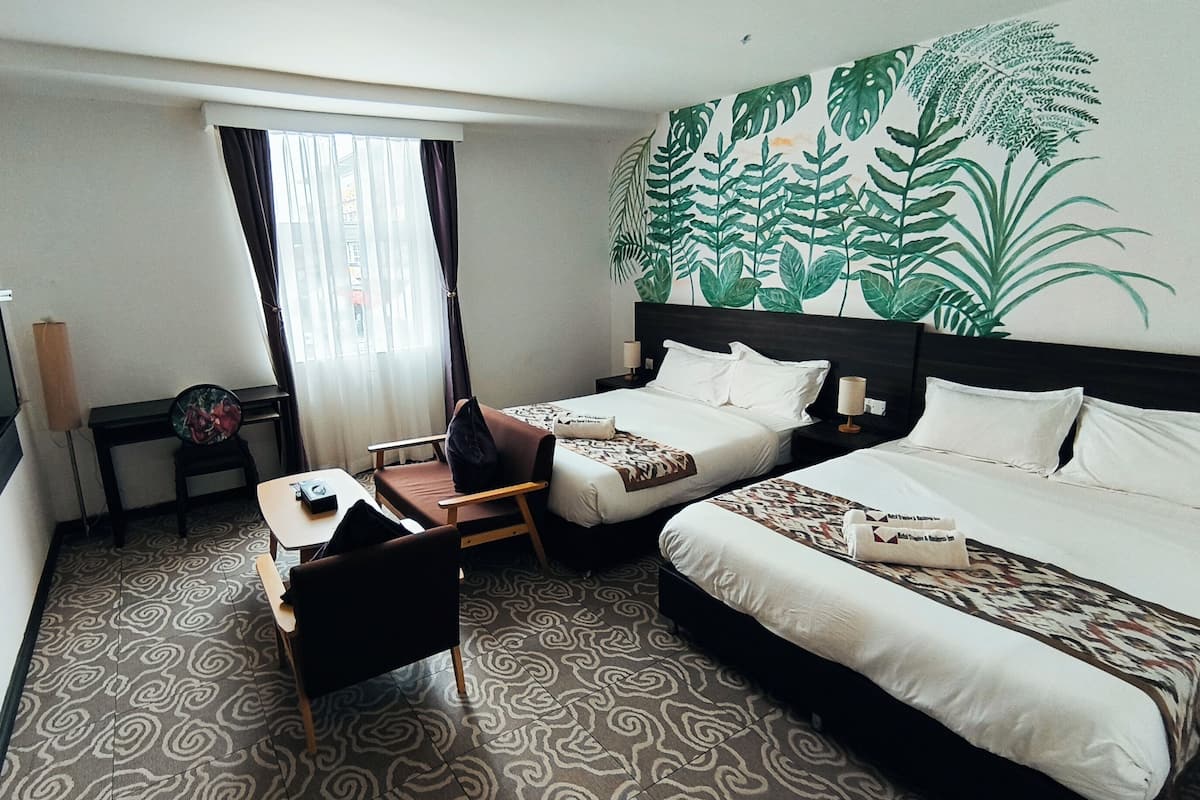 A hotel room with two beds, a desk, a chair, a TV, and a large plant on the wall.