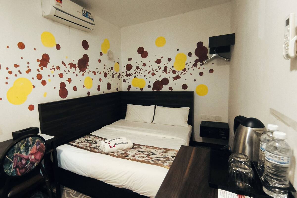 A hotel room with a bed, a desk, a chair, a water bottle, and a coffee maker.