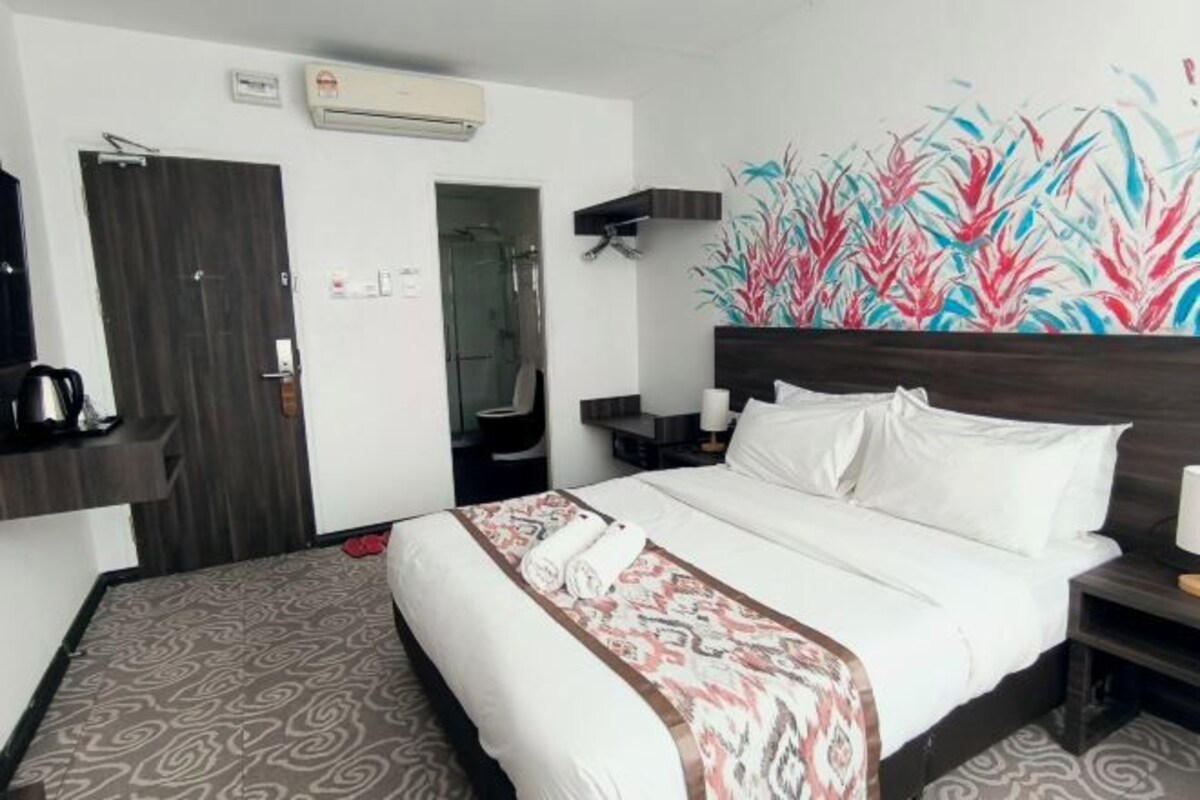 Una camera d'albergo con un letto, una doccia, una TV a parete e un quadro.