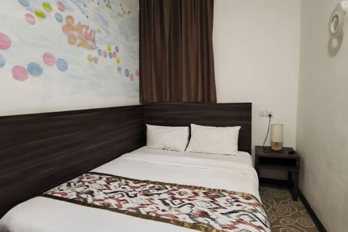 Camera d'albergo con un letto grande, una testiera, un comodino con una lampada e un muro decorato con un quadro astratto dai colori vivaci.