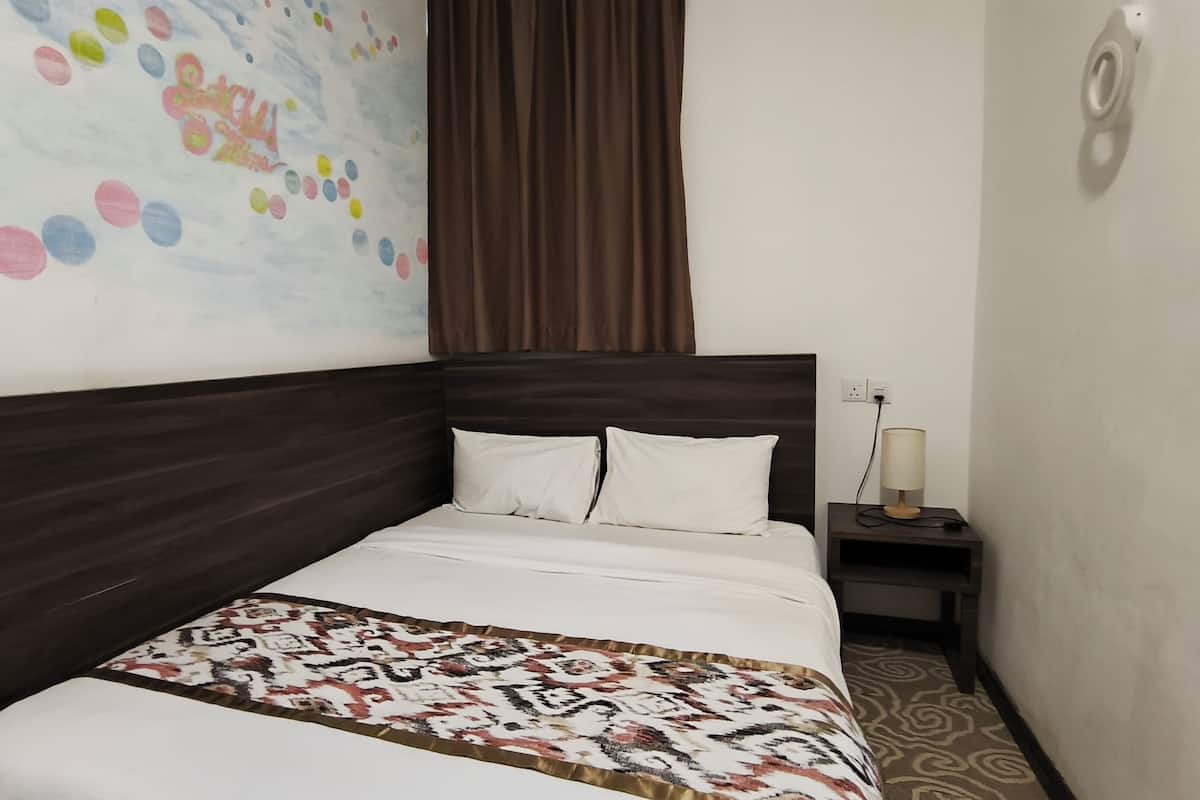 A hotel room with a large bed, a nightstand with a lamp, and a wall with colorful circular patterns.