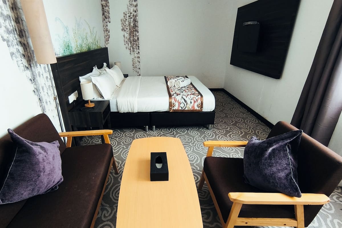A hotel room with a bed, two sofas, a table, a TV, and a patterned carpet.