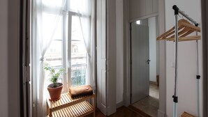 Una habitación con un banco, una planta en maceta, un perchero de madera y una puerta que da a otra estancia.