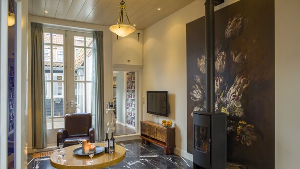 Een woonkamer met een open haard, een ronde tafel met kaarsen, een leren fauteuil en een aan de muur bevestigde televisie.