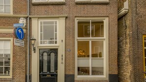Een tweelaags bakstenen gebouw met een zwarte voordeur, grote ramen en een straatnaambordje dat een afslag links aangeeft.