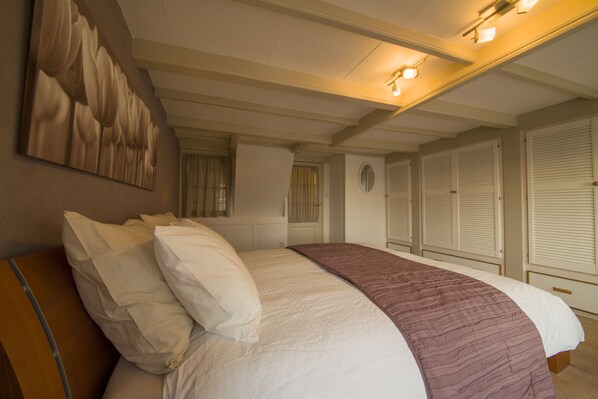 Un dormitorio con una cama grande, un cabecero, una obra de arte colgada en la pared y una ventana con cortinas.