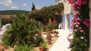A building with a garden area featuring potted plants and flowers, a pathway, and a view of the surrounding landscape. - Single storey studio, private swimming pool, secure parking (Callian)
