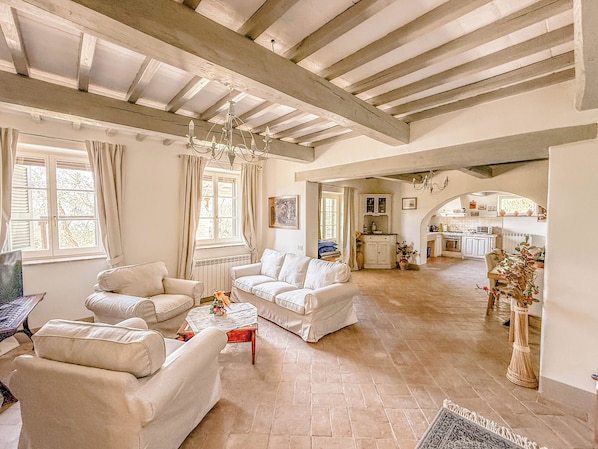 A spacious living area with a high ceiling, a fireplace, and a view into the kitchen.
