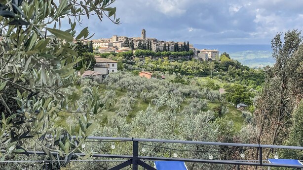 Vista panorámica de un pueblo costero con edificios históricos, olivares y cielo despejado.