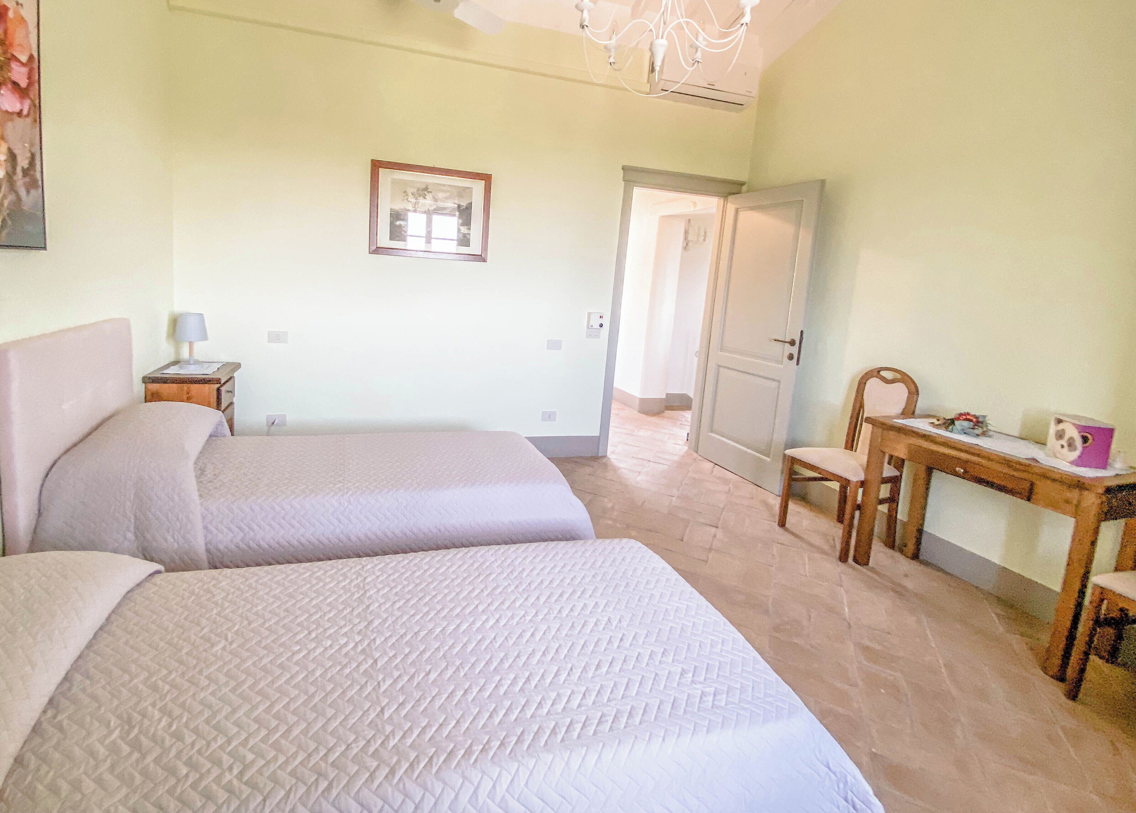 A bedroom with two beds, a desk, a chair, and a door leading to another room.