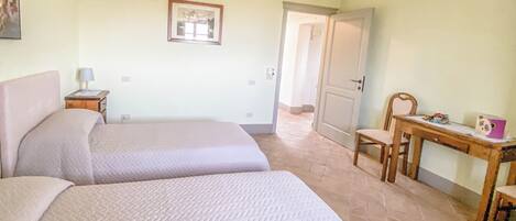 A bedroom with two beds, a desk, a chair, and a door leading to another room.