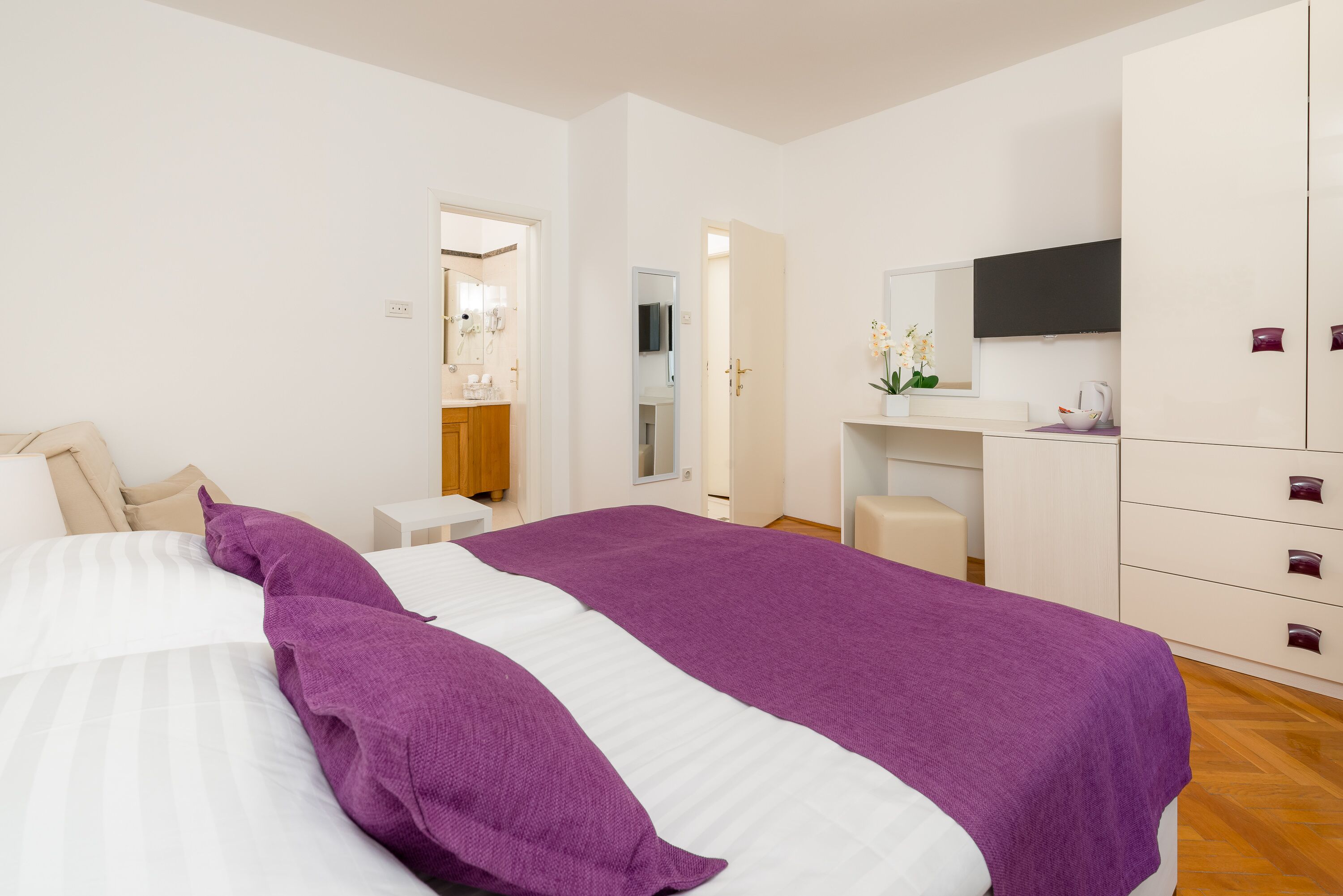 A bedroom with a large bed, a desk, a dresser, and a mirror.