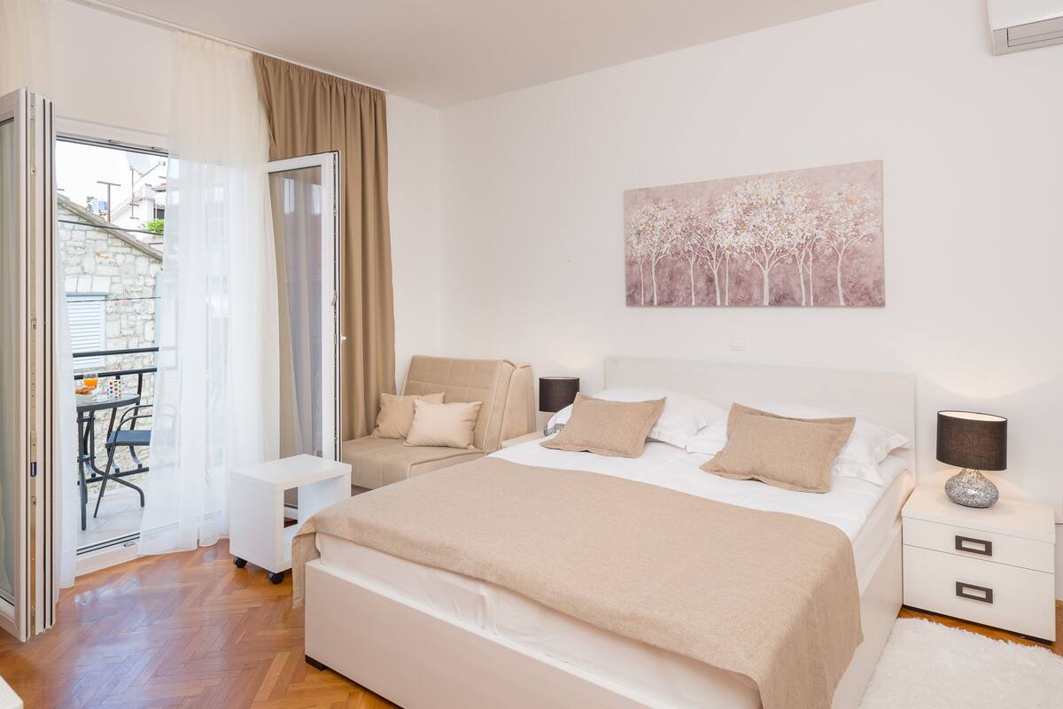 A bedroom with two beds, a small table, a chair, and a painting on the wall.