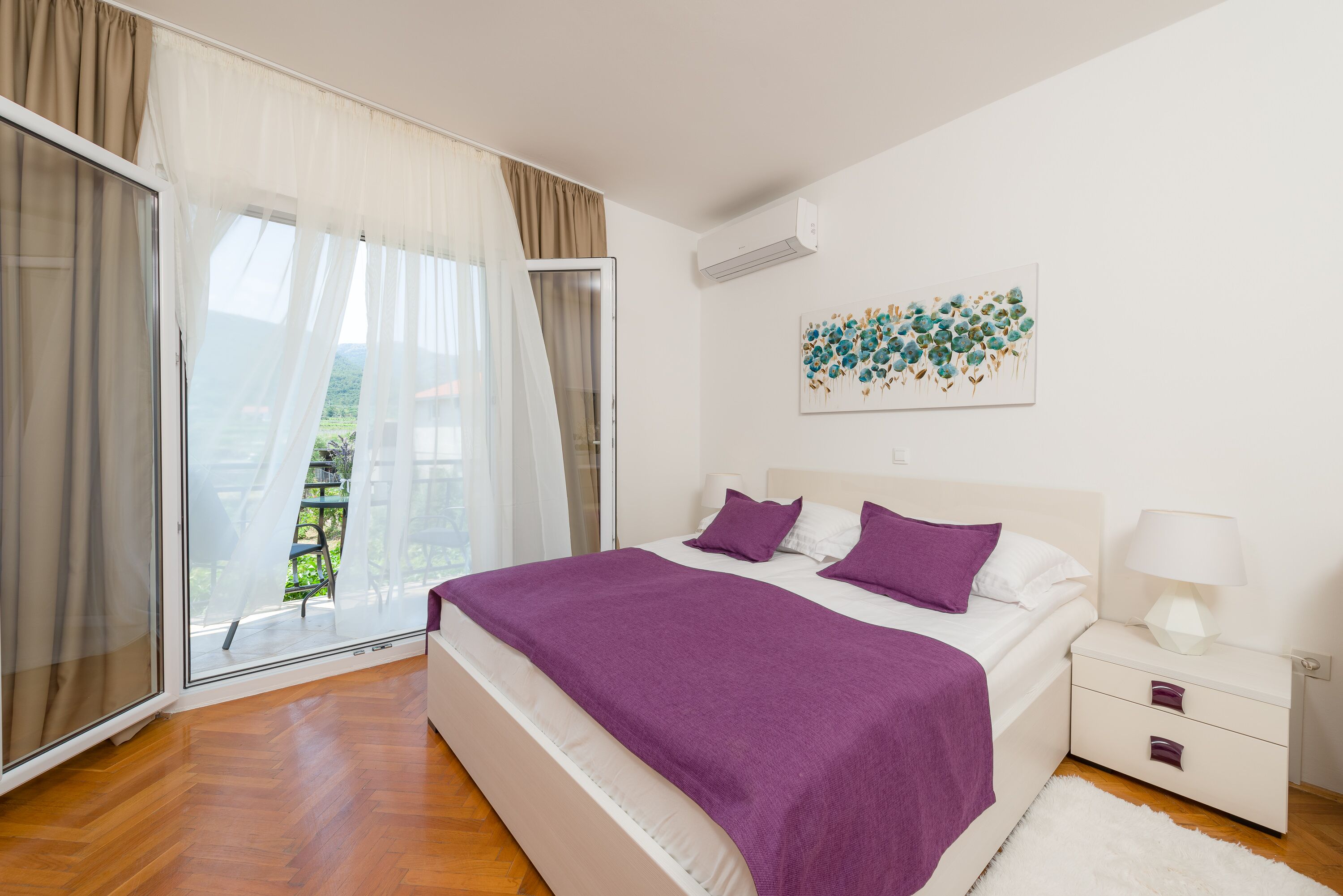A bedroom with a bed, a nightstand, a window with curtains, and a wall-mounted air conditioner.