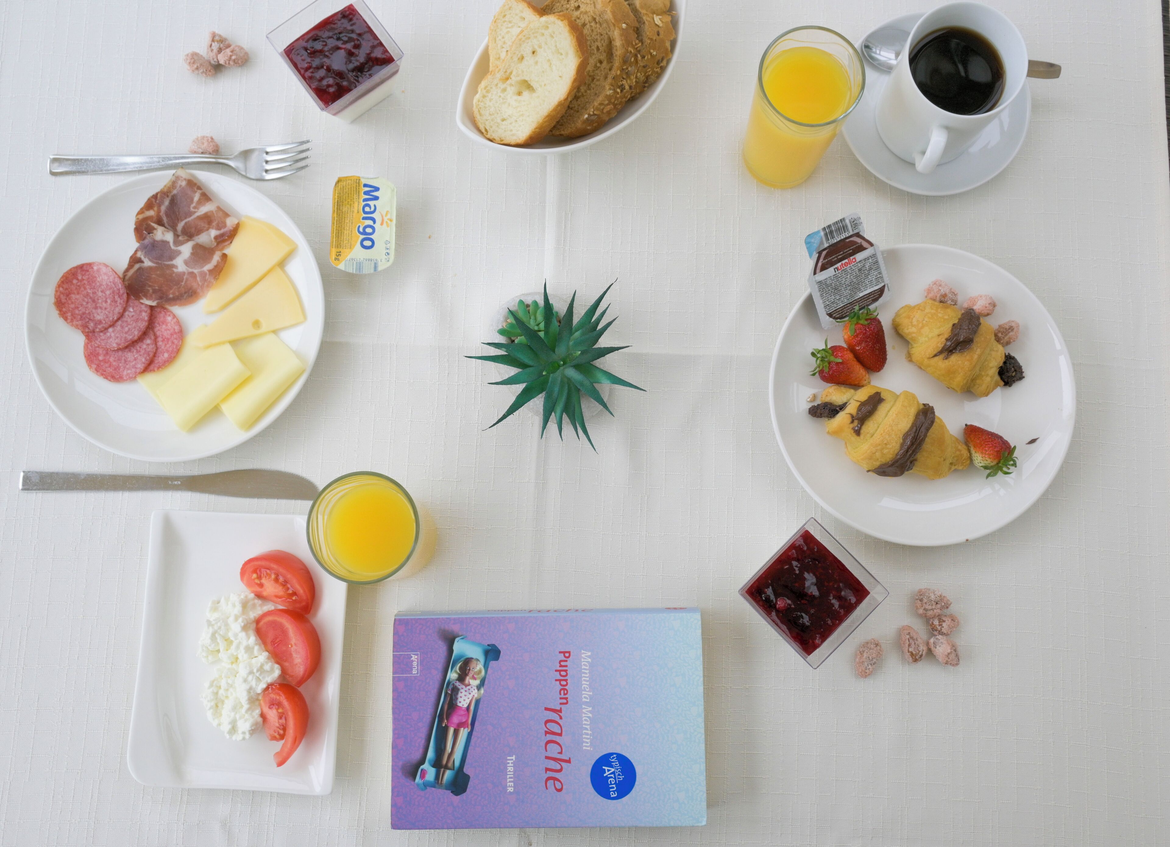 A breakfast table with various food items, a book, and a glass of juice.