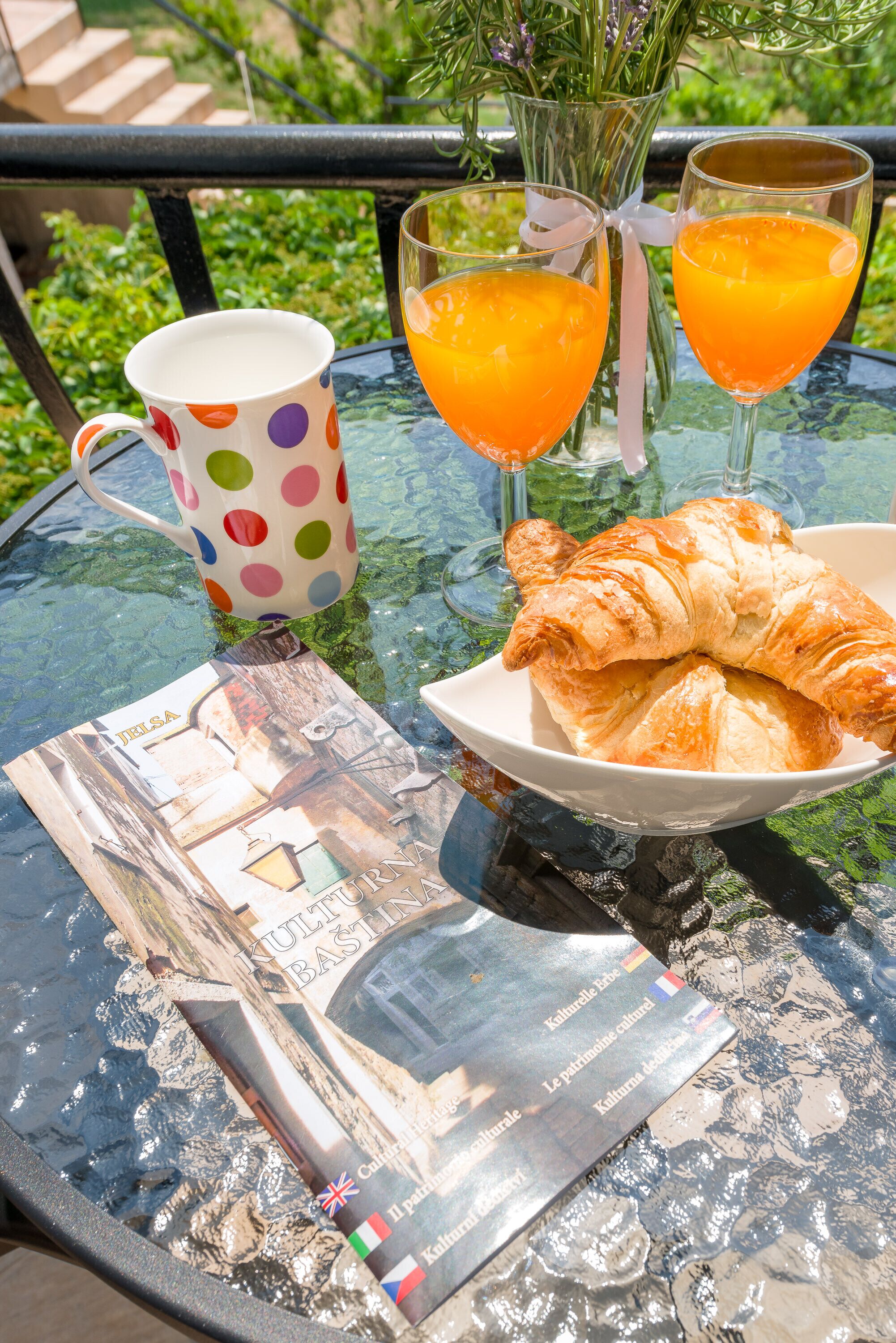 Una mesa con una taza de lunares, dos vasos de jugo de naranja, un plato con croissants y un folleto.
