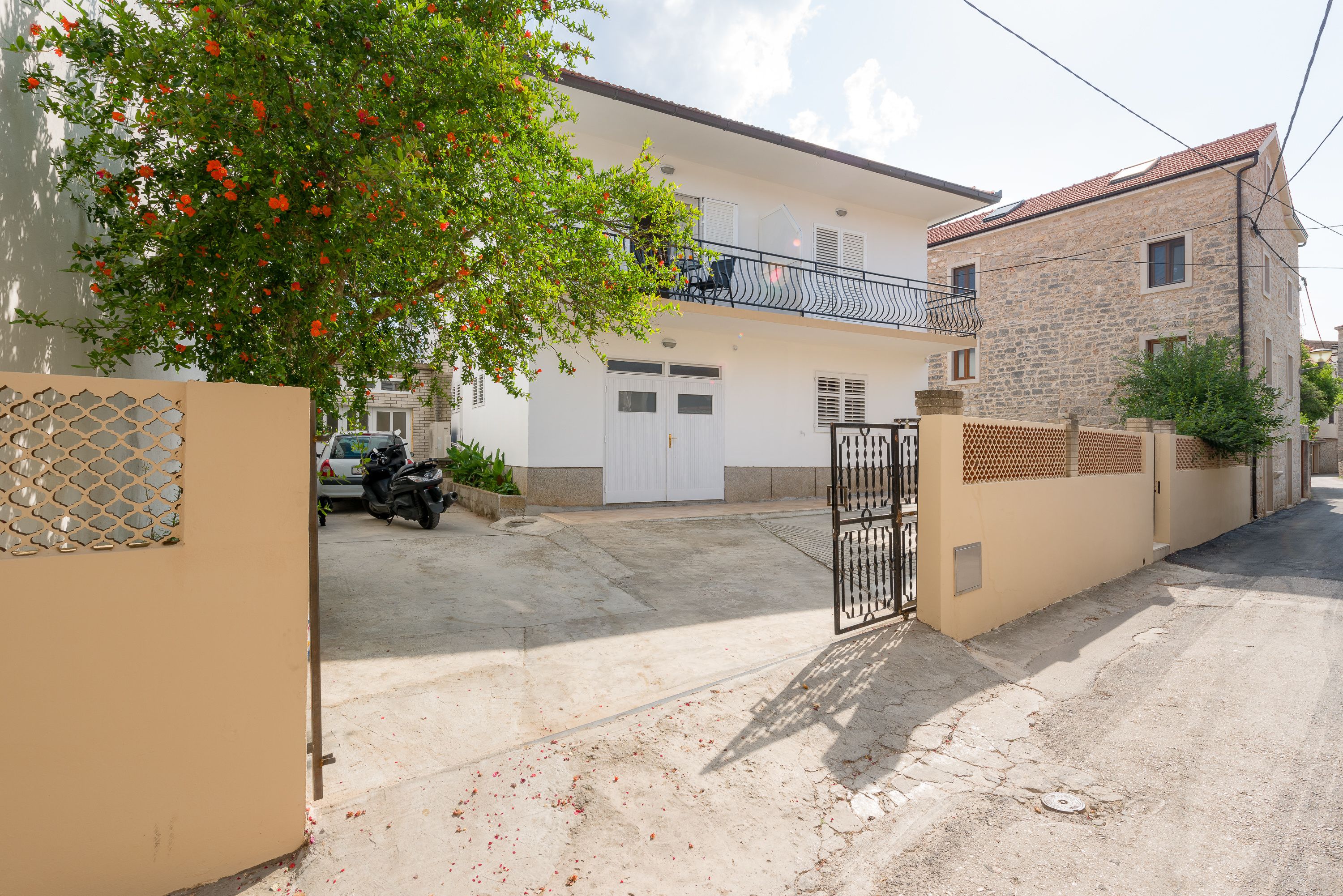 A two-story house with a white exterior, a balcony, and a gated entrance.